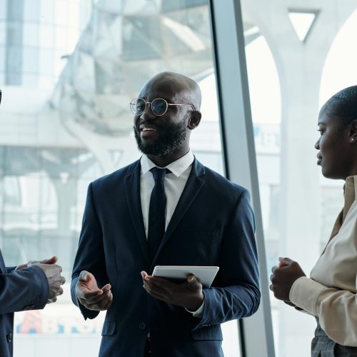 Group of three young African American employees in formalwear having discussion of ideas while preparing new business project